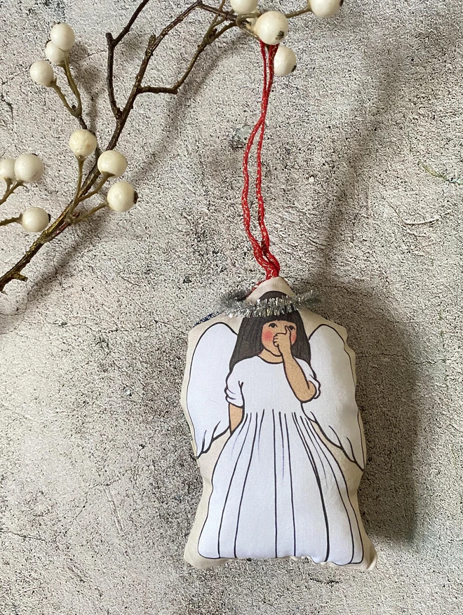 a little Christmas tree decoration featring printed illustrated fabric of a little brown skinned angel girl sucking her thumb with long dark hair and a small tinsel halo