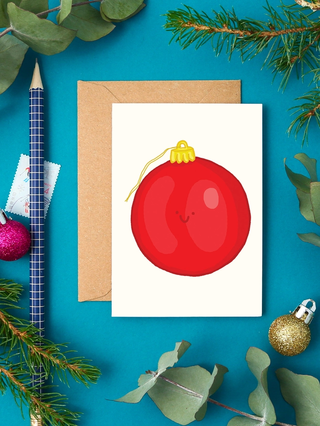 Illustration of a happy red Christmas bauble on a mini greeting card with kraft envelope