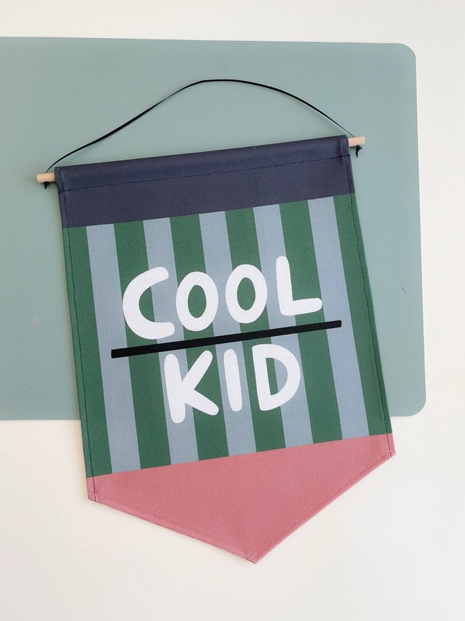 Blue and green striped wall banner with the words cool kid in white lettering