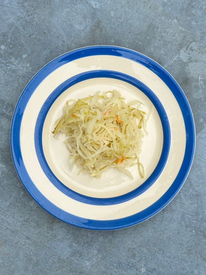 Muti Kraut On A Blue And White Plate Atop A Steel Topped Table.