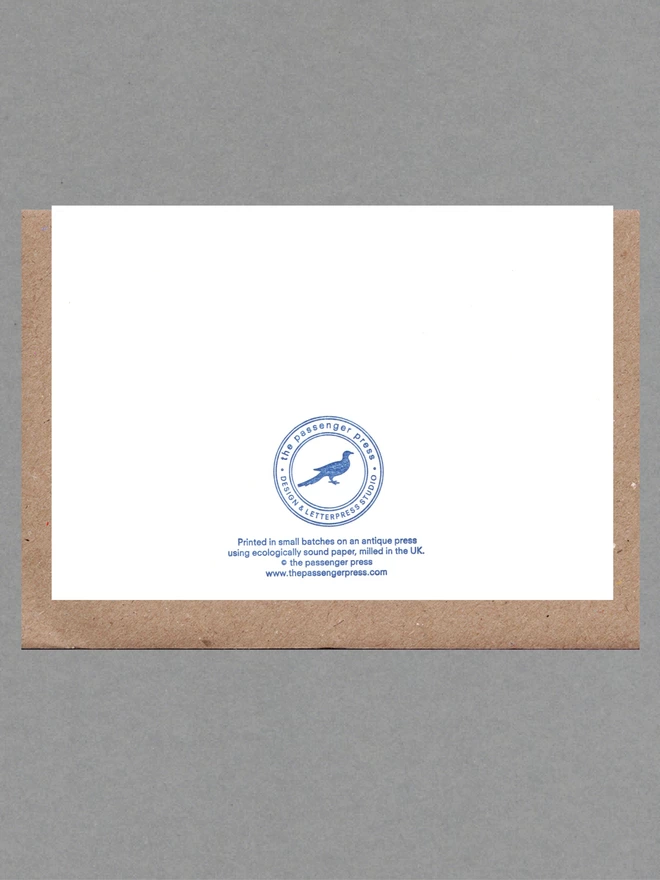 Back of white card with blue text on it with a brown envelope behind