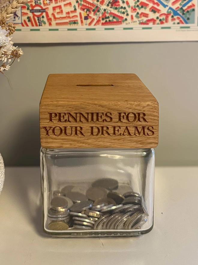 Oak money jar. A glass jar of coins with an oak lid engraved PENNIES FOR YOUR DREAMS and a coin slot in the top.