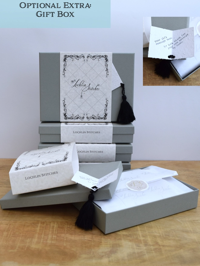 A soft grey gift box, approx. L178x W128x H32mm, with outer card casing, with white waxed tissue paper and a gift card embedded with seeds with a black tassel.