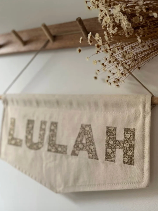 Patterned Letter Banner. A small banner with ‘LULAH’, hanging on a wall.