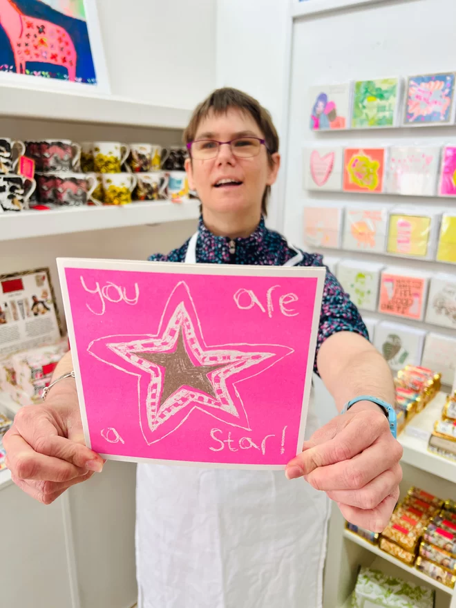 Artist holding a bright pink card with a gold star and the words You Are A Star!