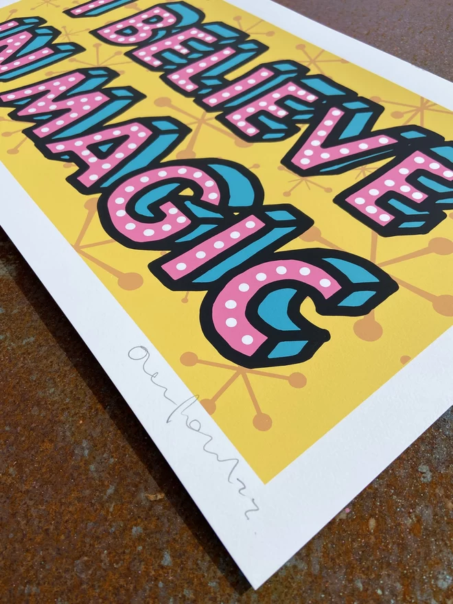 "I Believe In Magic" Hand Pulled Screen Print rectangular 1950s pattern background in deep yellow with the words i believe in magic printed on top in hand drawn lettering pink writing black outline 