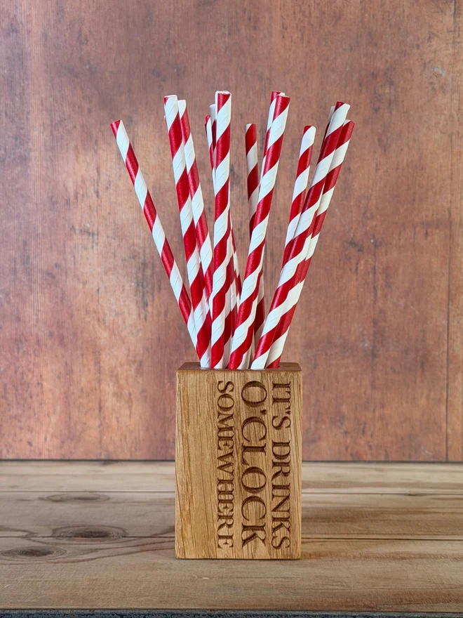 Stripy straws in a straw cup with engraving that says It's drinks o'clock somewhere...