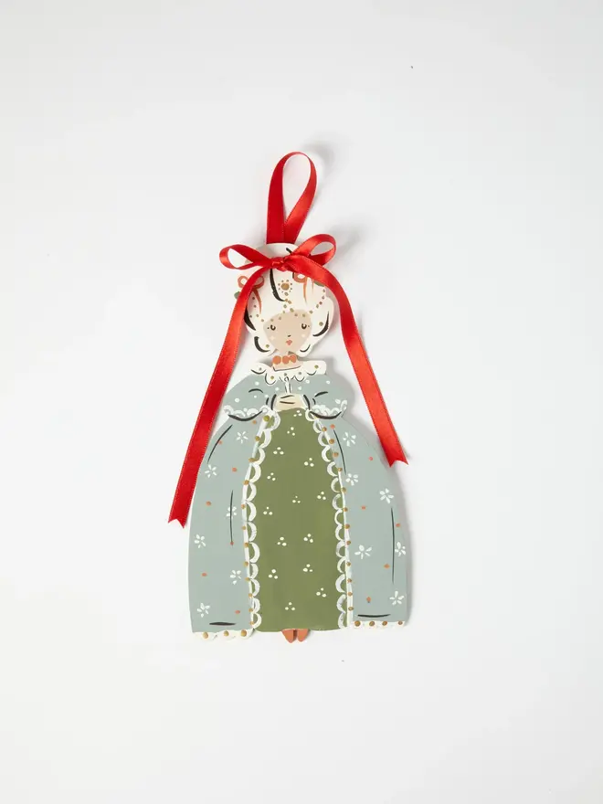 Sorrel Princess Tree Dancer. a flat lay product shot of the sorrel princess tree dancer hanging ornament on a plain white background, showing a princess figure with an elaborate powdered wig decorated with pearls and jewels. she wears a sage green gown with an olive skirt panel, trimmed with white lace and scalloped detailing, and hangs from a red satin ribbon tied in a bow. hand-painted floral and dot detailing gives the ornament a folk-art, storybook charm.