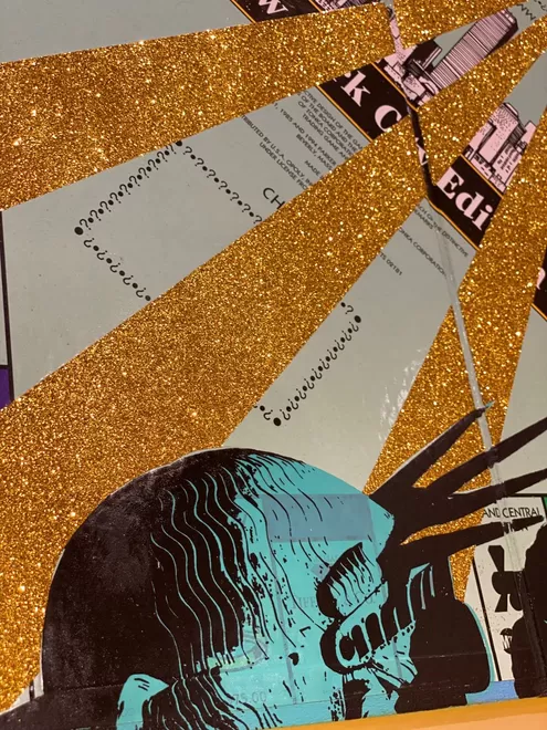 Cross section of a Monopoly board close up with the back of the head of the Statue of Liberty printed on it and gold glitter stripes 