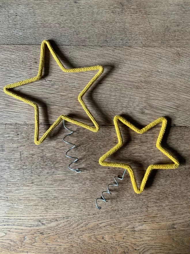 A small and a large gold string covered wire star with a coil for topping a Christmas tree on an oak table