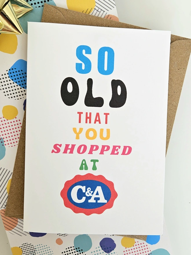 A photograph of the front of a humorous A6 greeting card illustrated using brightly coloured text and the retro shop logo. The text says so old you shopped at C&A.
