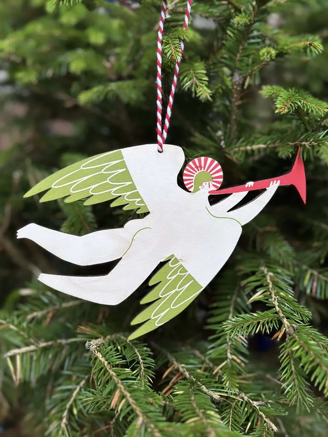 wooden, handprinted angel blowing a trumpet, hangs on a green christmas tree