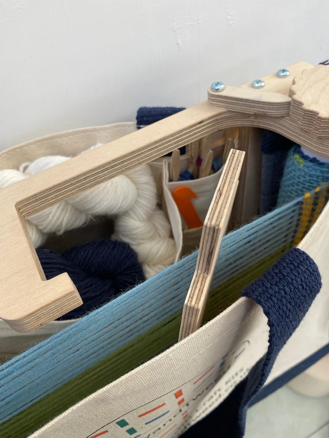 The inside of a TabbyandTweed project bag showing the side of a wooden loom and some white and navy yarn