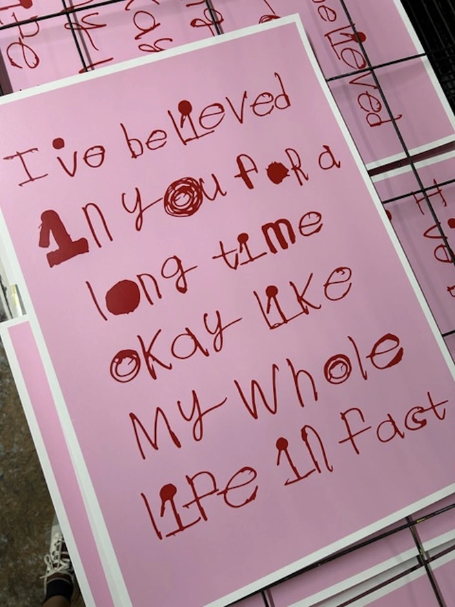 Pink screen print with red font that fills the page drying on the rack after being freshly printed