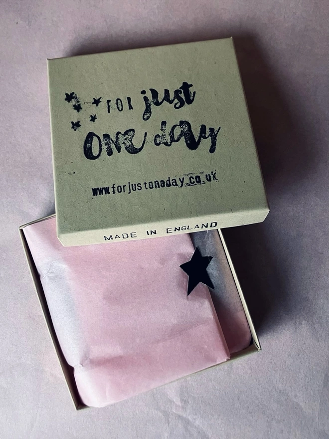 Brown box with pink tissue paper a black star and for just one day on the top