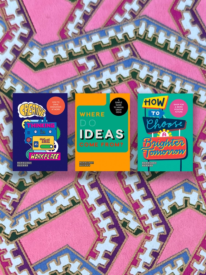A set of three illustrated maps with colorful covers, titled 'Creative Thinking in The Workplace', 'Where Do Ideas Come From?', and 'How to Choose a Brighter Tomorrow'. The books are laid out in a row with their spines facing forward and on a multi-coloured and multi-patterned background.