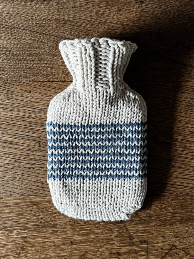 Mini Hot Water Bottle with navy striped knitted string cover on an oak table