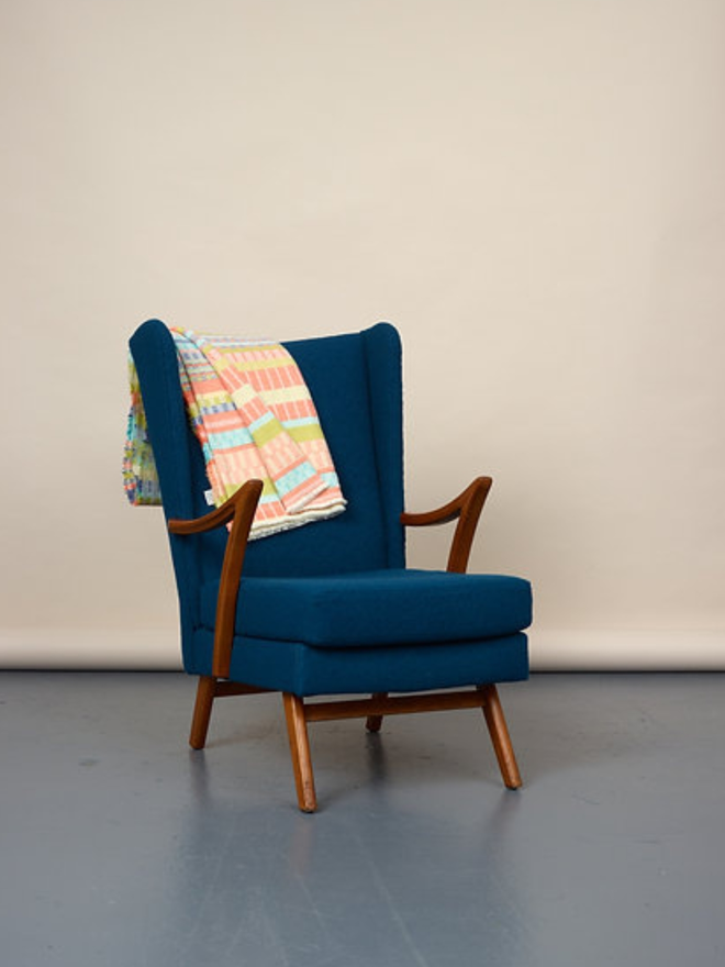 indie lambswool blanket. a multicoloured blanket photographed thrown over a blue chair.