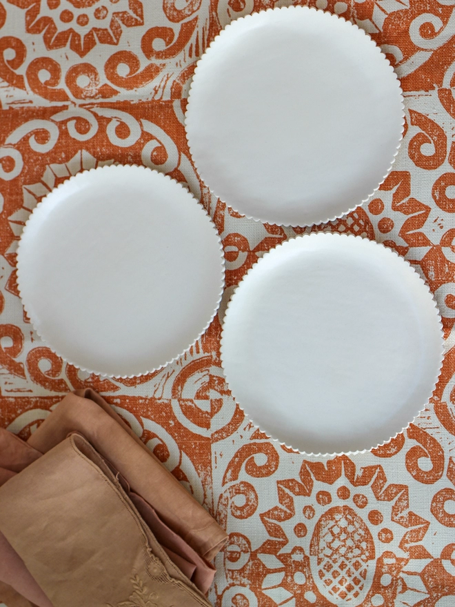 three white plates with scalloped edges on a printed orange and white cloth