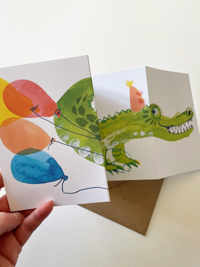 Esther Kent illustrated concertina greeting card showing a creen crocodile on a white background, with colourful balloons