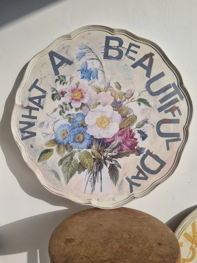 Art Panel made from a 'pie crust' table top. A pale background with mauve flowers and writing in mauve that says 'what a beautiful day'.