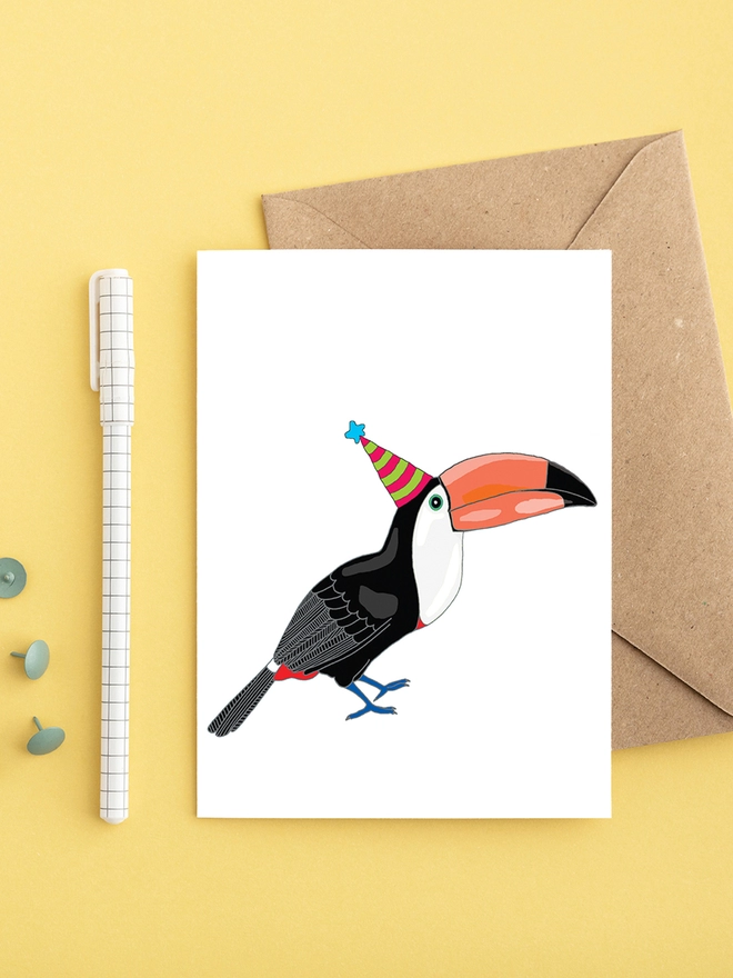 Bright greeting card featuring a toucan in a hat