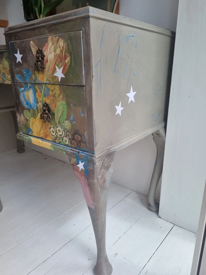 Vintage painted dressing table and chair. Painted in coffee grey and decorated using layered antique florals with yellow and blue accents and finished with hand-cut white paper stars. Text reads in blue 'think happy thoughts'. Heavily distressed finish.