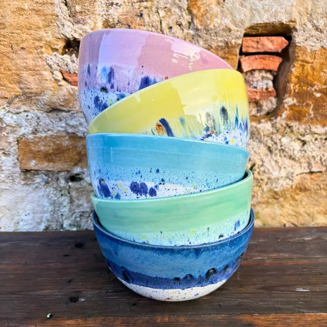Shoreline Ramen Bowl, a collection of colourful ramen bowls stacked together on a wooden surface against a brick backdrop. 