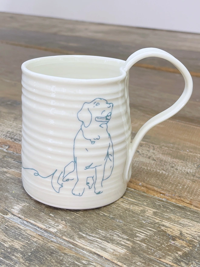 hand thrown porcelain mug with blue line drawing of a golden retriever on the side sitting atop a rustic table