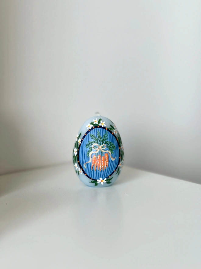 Hand Painted Easter Egg Candle Carrots Bunch, an Easter egg candle sitting on a plain surface. It's Easter and floral design wraps around it. 