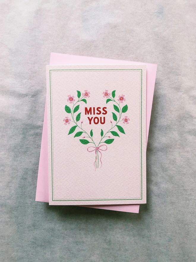 Pink floral flower garland tied with a pink ribbon surrounding hand lettering "Miss You" Friendship card