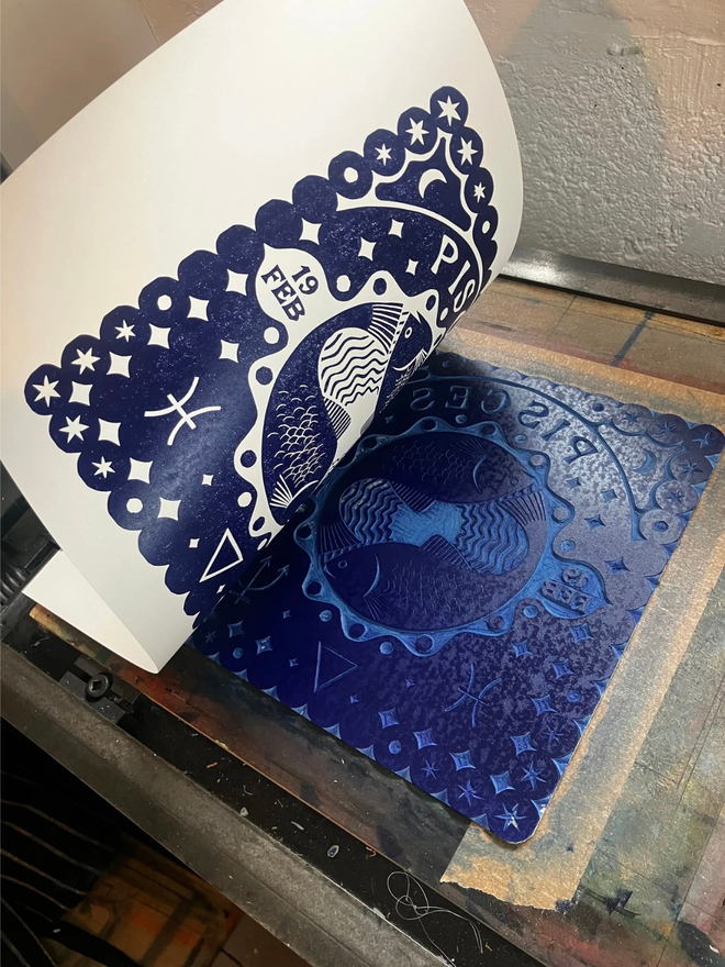 pisces zodiac linocut. linocut fish and zodiac symbols printed on a blue background.