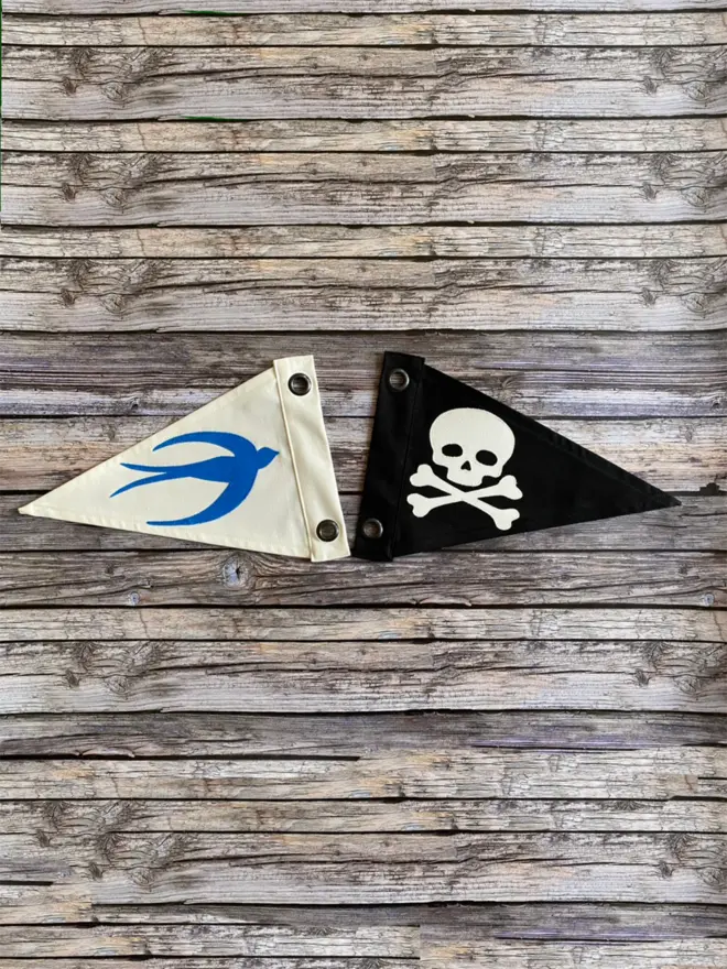 two pennant flags. one ivory with a blue swallow on and one black with an ivory skull and crossbones on.
