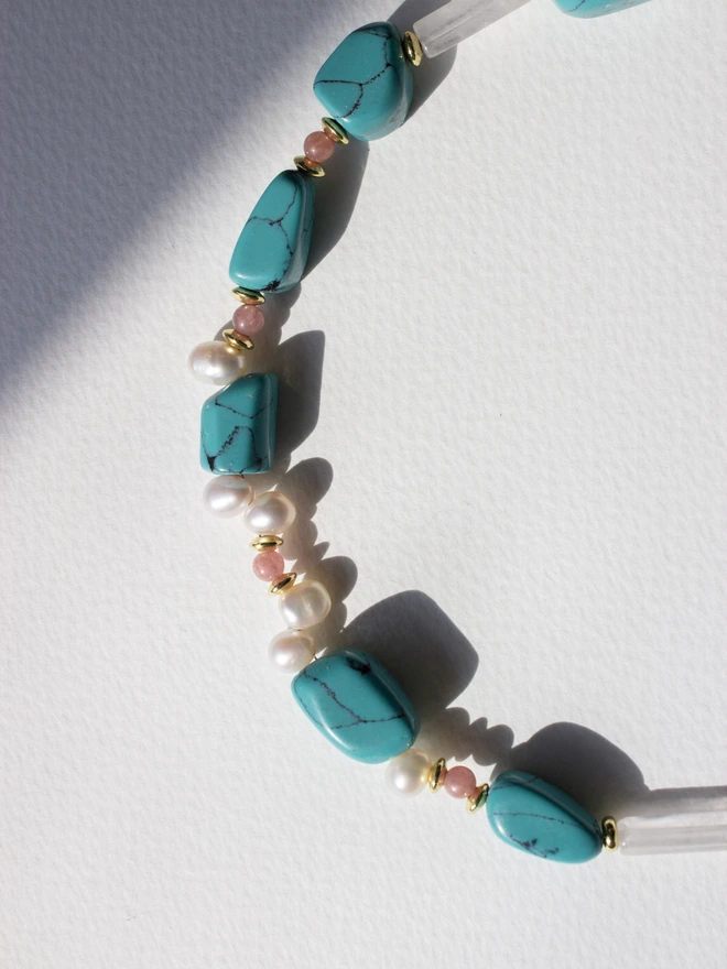 Necklace with turquoise, rose quartz and pearl beads on a white background