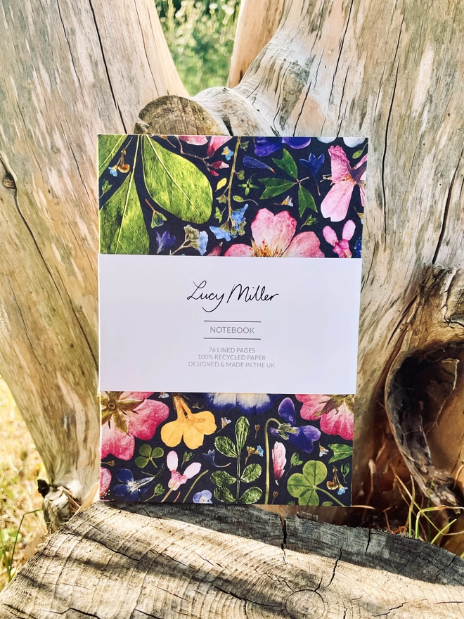 Recycled Notebook with Pressed Flower Patterned Cover, 'Lucy Miller' Branded Belly Band, Leaning Against Tree Trunk