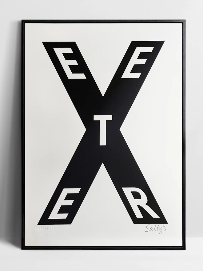 Framed print of Exeter, arranged as the letters EETER within the big letter X, leant against a white background.