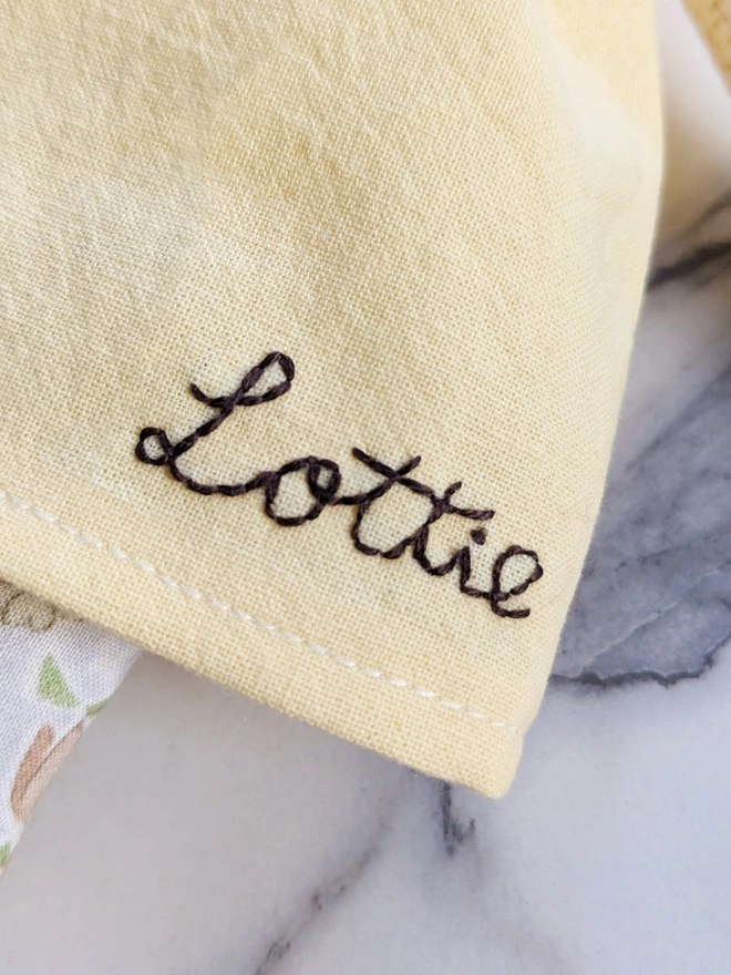 Handmade heirloom doll's soft yellow dress with hand embroidery 'Lottie' on it.