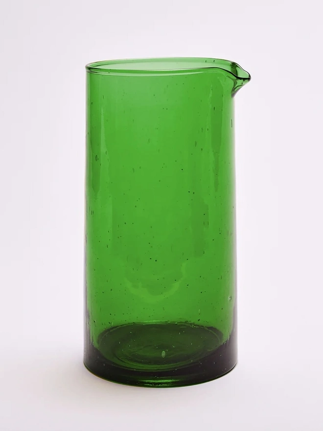 Glass Carafe, a large green glass jug sitting  against a plain backdrop. 