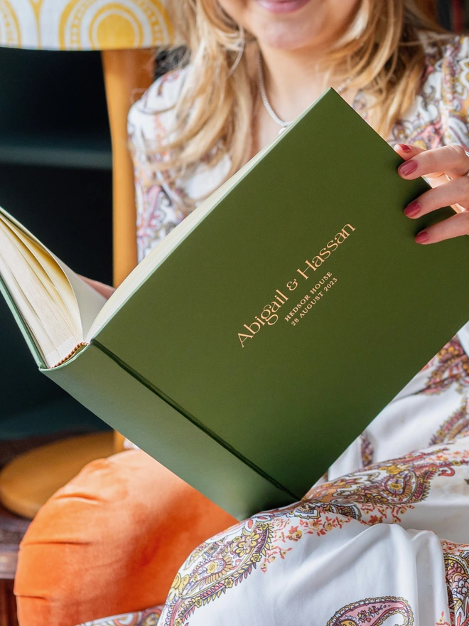 A woman holds open and reads a Large Wedding Photo Album Personalised With Bespoke Printing with a green cover.