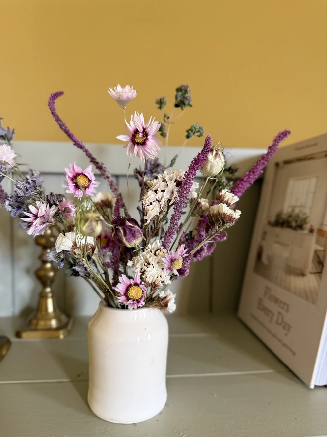 a selection of dried flowers in a ceramic vase on a shelf with candles in brass candlesticks