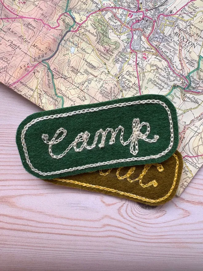 Two custom chain stitch embroidered patches in green and willow laying on a vintage map