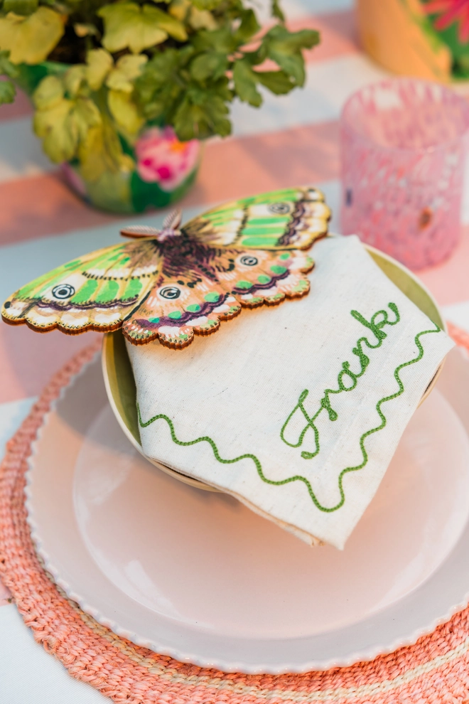 Personalised linen napkins with moss green, 'Frank' folded into a tablescape with pink and peach placemates and plates on a pink and white striped tablecloth