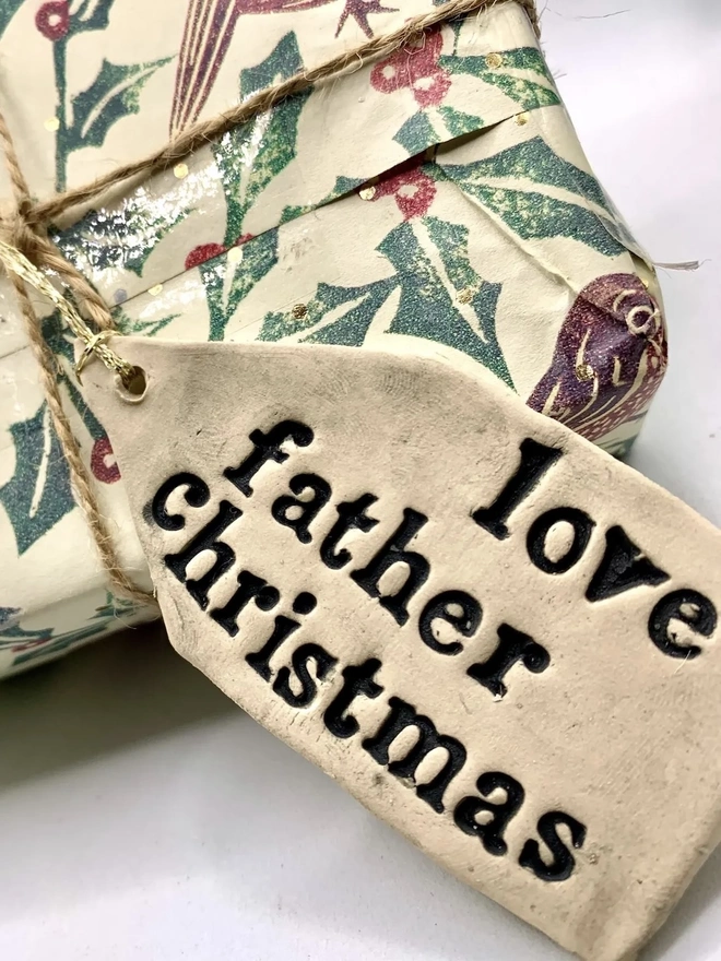 'Love Father Christmas' Handmade Ceramic Gift Tags, a ceramic gift tag attached to a gift sitting on a plain white surface. 