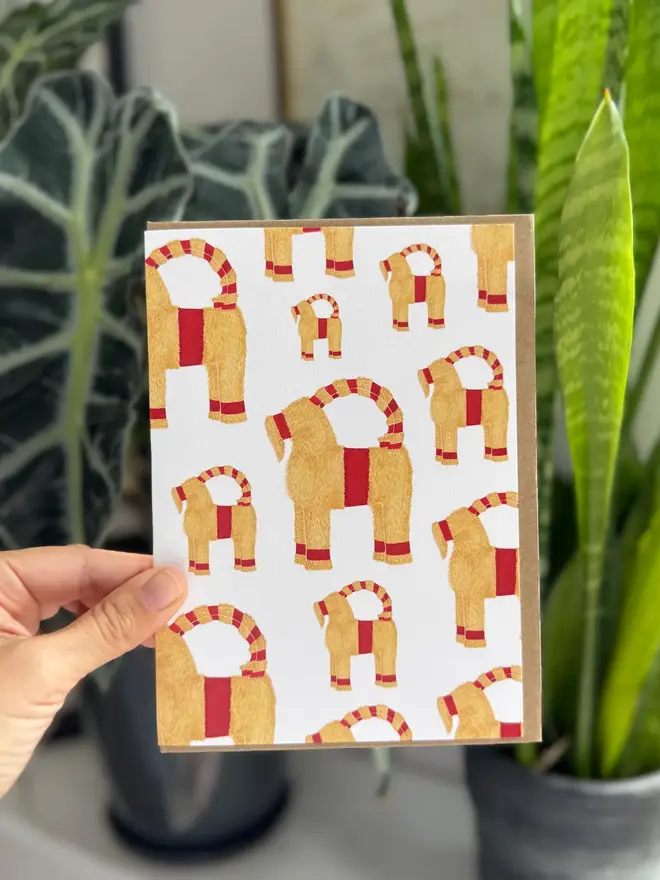 A straw goat christmas greeting card with a backdrop of plants 