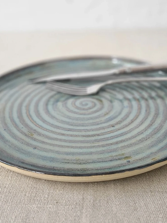 Classic Ceramic Dinner Plate, a colourful ceramic dinner plate sitting on a plain surface. It is accompanied by some cutlery. 