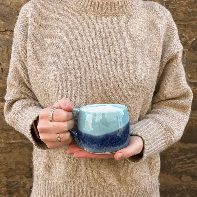 Landscape Large Round Mug, a person in a jumper holding a colourful coffee mug in front of them. 