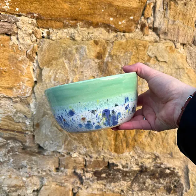 Shoreline Ramen Bowl, a person holding a colourful ramen bowl against a brick backdrop. 