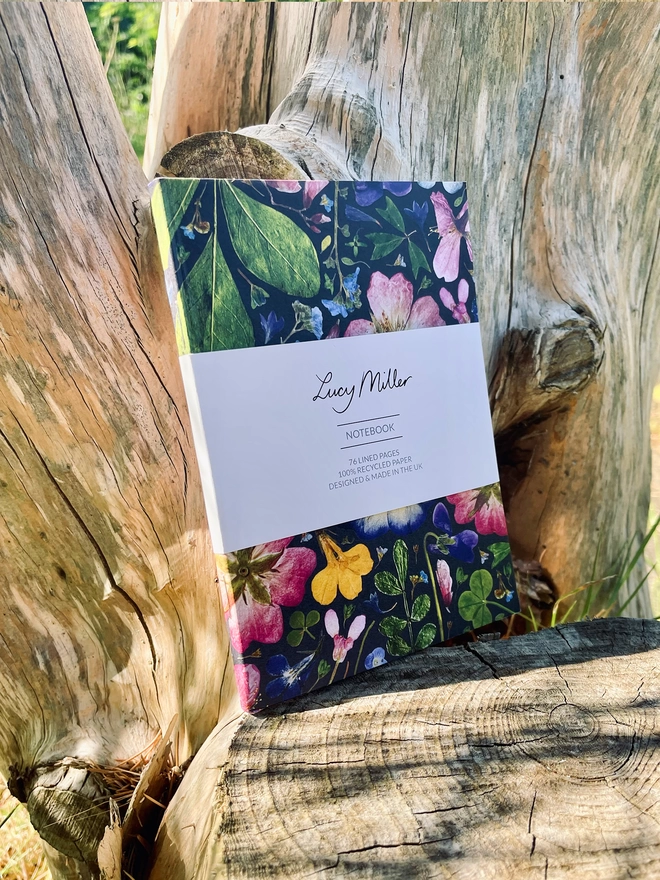 Eco-friendly Notebook with Botanical Print Cover with wildflowers, Stapled Spine, 'Lucy Miller' Branded Belly Band, Leaning Against Tree Trunk