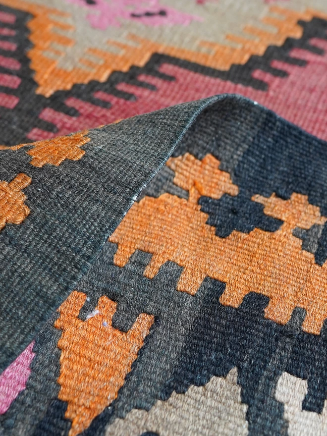 Orangey, red and black geometric vintage kilim hand woven rug on wooden floor in maximalist dining room with green woodwork