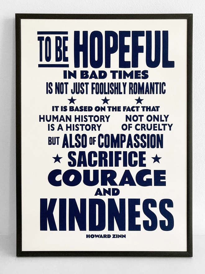 Framed typographic print of a quote by Howard Zinn. It reads "To be hopeful in bad times is not just foolishly romantic, it is based on the fact that human history is a history not only of cruelty but also of compassion, sacrifice, courage and kindness". Navy blue text on white paper.
